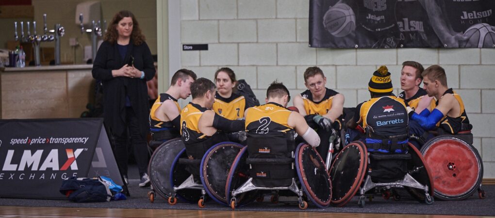 A team of wheelchair rugby players gather round for a meeting.