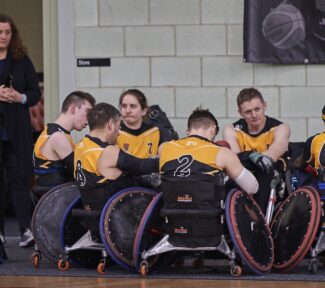 A team of wheelchair rugby players gather round for a meeting.