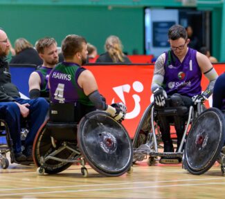 A team in purple vests called the 'Hawks' gather round to discuss team tactics during a game
