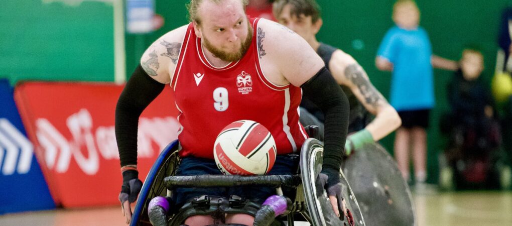Wheelchair Rug y Player pushing with ball on lap.