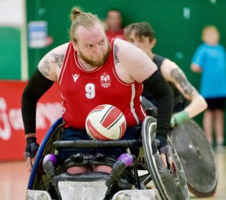 Wheelchair Rug y Player pushing with ball on lap.