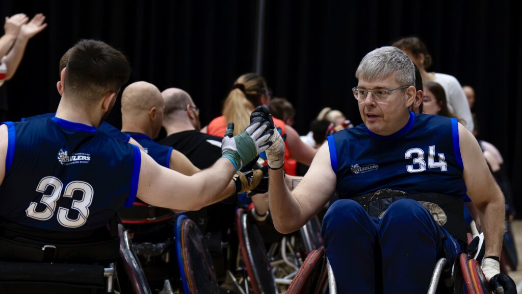Two teams of wheelchair rugby players shaking hands after a game of wheelchair rugby