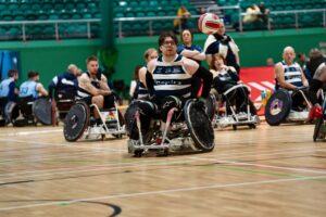 wheelchair rugby layer pushing hard and trying to catch a ball. in a white and blue vest.