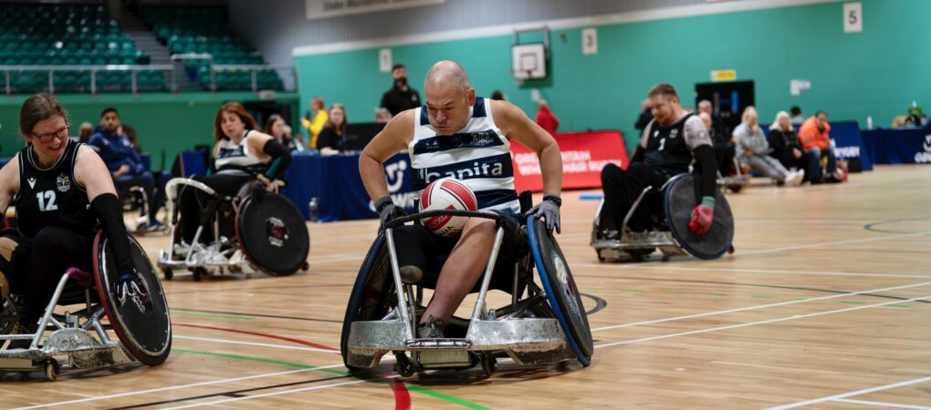 wheelchair rugby layer pushing hard in a white and blue vest.