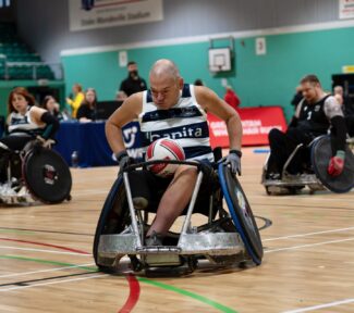 wheelchair rugby layer pushing hard in a white and blue vest.