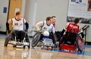 female wheelchair rugby player carrying the ball through defenders.