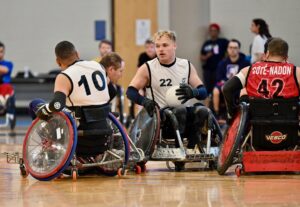 Male wheelchair rugby player carrying the ball wearing a white vest.