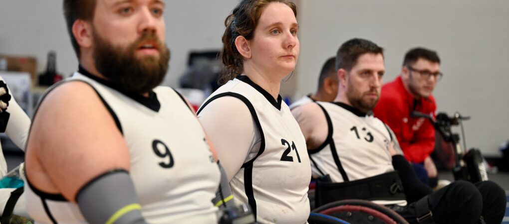 3 wheelchair rugby players watching a game. all wearing white vests