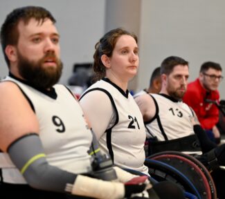 3 wheelchair rugby players watching a game. all wearing white vests