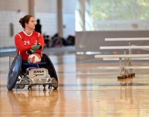 fmeale wheelchair rugby player with a ball on her lap resting and watching intently